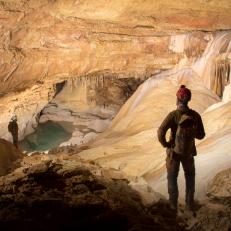 Travis and Brad Wuest beyond the well shaft pit in a room with a lake and huge flowstones.