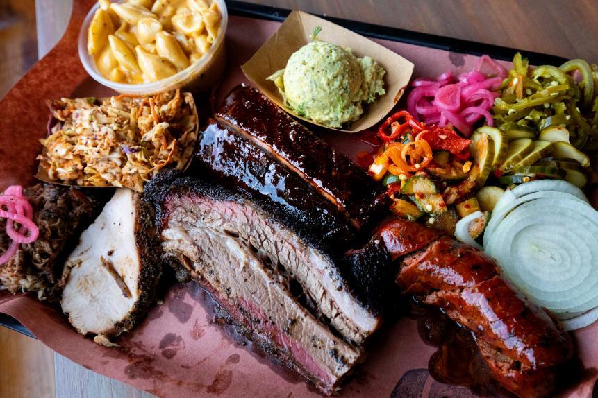 A plate of mouthwatering barbecue with brisket, sausage, potato salad, and so much more from la Barbecue in Austin, Texas.  LeAnn Mueller with the help of her wife Alison Clem run la Barbecue with recipes and flavors inspired by their travels around the world.