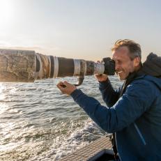 Photographer Ian Shive holds up his massive camera and lens on a boat to try and photograph the native Texas Whooping Crane in Aransas National Wildlife Refuge, Texas. These cranes travel over 2,5000 miles each year to winter in Texas on the 115,000 acre refuge.