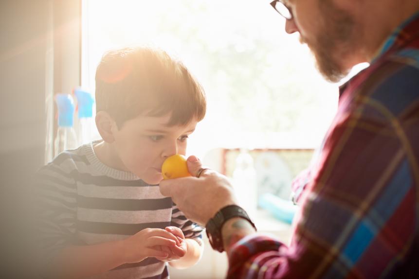 A father holding a lemon up to his son so he can smell it