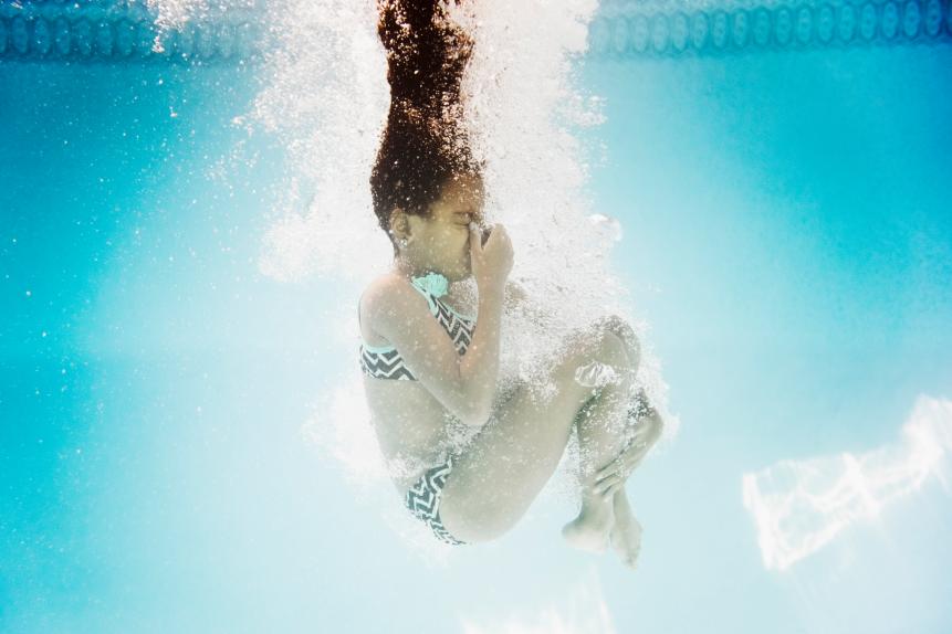Hispanic girl swimming underwater holding nose