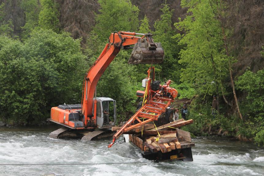 Excavator removing woodmizer from truck over River.
