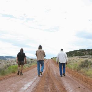 Chad Ollinger, Duane Ollinger, and Charlie Snider walk down the dirt road, away from camera, at Blind Frog Ranch.