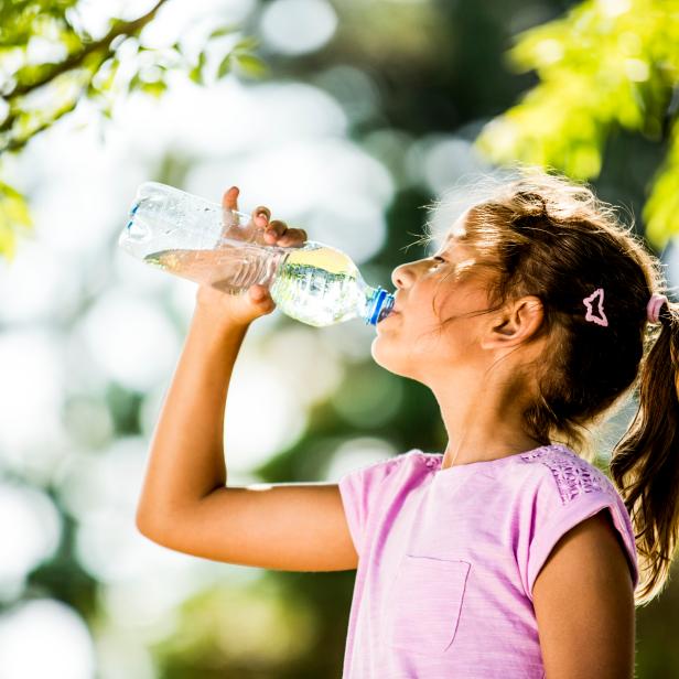 Girl drinking water from plastic bottle in park.