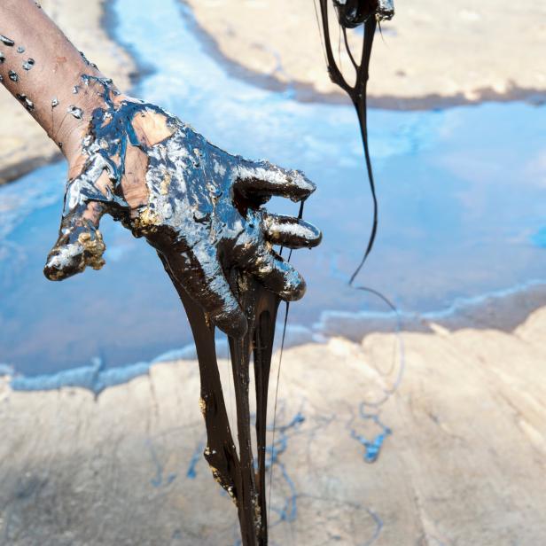 Oil spills over hand and river in Venezuela.