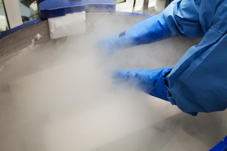 Doctor in hazmat suit working with container with embryonal cells in liquid nitrogen