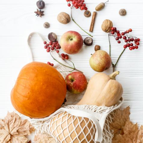 Reusable shopping bag with pumpkins, apples, berries, nuts and autumn leaves on white wooden background. Eco friendly Thanksgiving, flat lay. Zero waste holidays, fall harvest