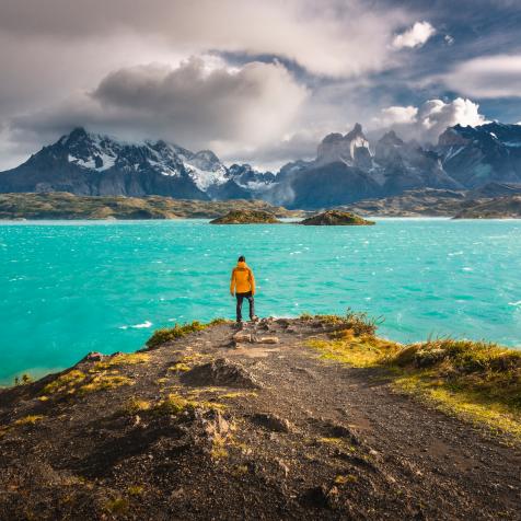 One man standing on top of a headland over lake Pehoe admiring the Cuernos del Paine and Paine Grande peaks on a windy day, Chilean patagonia