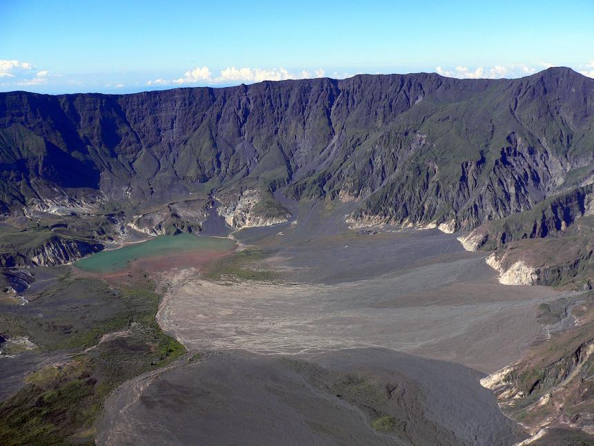 An aerial view looking into Tambora Volcano from the rim of the caldera, on the island of Sumbawa in Indonesia. The 1815 Tambora eruption is the largest observed volcanic eruption in recorded history.  The explosion was heard 2,600 km away, and ash fell at least 1,300 km away.  Pitch darkness was observed as far away as 600 km from the mountain summit for up to two days. Pyroclastic flows spread at least 20 km from the summit. Due to the eruption, Indonesia's islands were struck by tsunami waves reaching heights up to 4 metres.   
An estimated 41 cubic km of pyroclastic trachyandesite were ejected, weighing about 10,000 million tonnes. This has left a caldera measuring 6â  7 km  across and 600â  700 m deep.  Before the explosion, Mount Tambora was about 4,300 m high, one of the tallest peaks in the Indonesian archipelago.  After the explosion, it measured only 2,851 m (about two thirds of its previous height).
The eruption column lowered global temperatures, and some experts believe this led to global cooling and worldwide harvest failures, sometimes known as the Year Without a Summer.  The eruption resulted in an estimated 100,000 deaths.