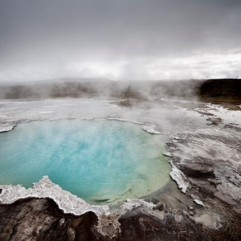 steaming geyser in iceland. the water is colored by algae.