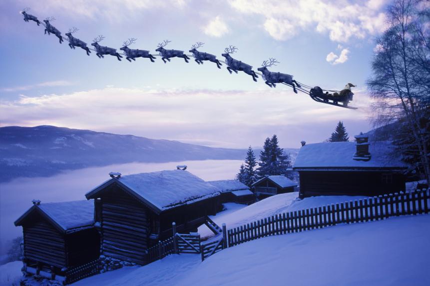 Santa Clause and his reindeer flying above an old farm covered with pristine snow