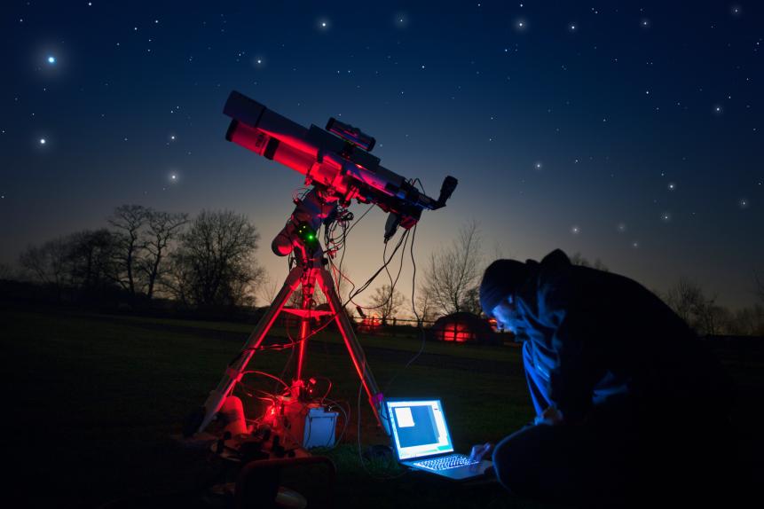 An amateur astronomer guides his telescope via a laptop while photographing the night sky.