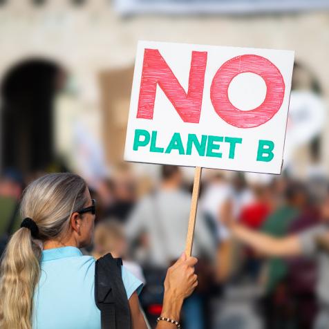 woman holding no planet b sign at protest march demonstration against climate change in european city, shallow focus, background blurred