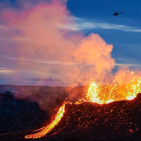 TOPSHOT - A helicopter flies near above the lava flowing from a fissure near the Fagradalsfjall on the Reykjanes Peninsula in Iceland on ,April 6, 2021. - The volcanic eruption, which has been ongoing for more than two weeks in Iceland about 40 kilometers from Reykjavik, spread on April 5, 2021 with a new fault spewing lava, according to the meteorological institute. (Photo by Halldor KOLBEINS / AFP) (Photo by HALLDOR KOLBEINS/AFP via Getty Images)