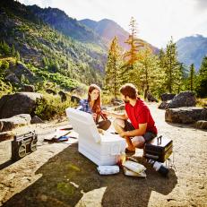 Couple setting up evening picnic site in wilderness toasting each other with beer bottles