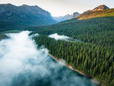 A drone photo created while flying over Hyalite Reservoir in the Gallatin Mountains of Montana. The sun is just beginning to rise and fog covers much of the lake