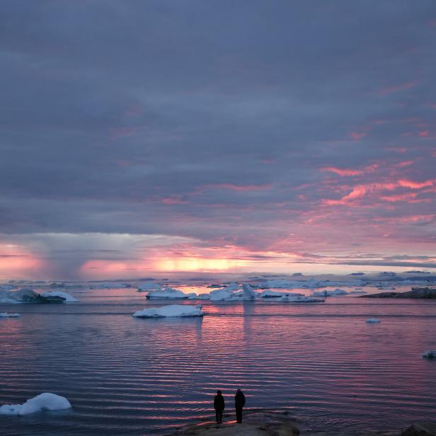 ILULISSAT, GREENLAND - SEPTEMBER 04: People watch the sunset as rain falls in the distance beyond floating ice and icebergs in Disko Bay on September 04, 2021 in Ilulissat, Greenland. 2021 will mark one of the biggest ice melt years for Greenland in recorded history. Researchers from Denmark estimated that in July of this year enough ice melted on the Greenland Ice Sheet to cover the entire state of Florida with two inches of water. According to NASA, Greenland has melted 5 trillion tons of ice over approximately the past 15 years, enough to increase global sea level by nearly an inch. The observations come on the heels of the recent United Nations report on global warming which stated that accelerating climate change is driving an increase in extreme weather events. (Photo by Mario Tama/Getty Images)