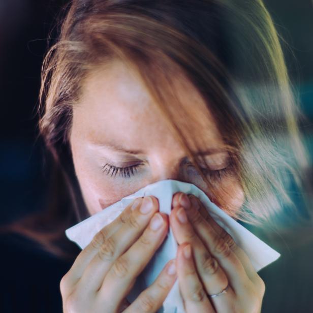 Woman sneezing behind a window, using a tissue.