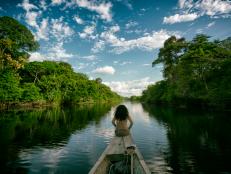 Sailing in a wooden boat on the Amazon river in Peru. An indigenous girl sitting on the front of the boat whilst sailing down the river.
