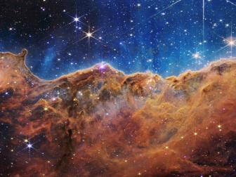 This landscape of “mountains” and “valleys” speckled with glittering stars is actually the edge of a nearby, young, star-forming region called NGC 3324 in the Carina Nebula. Captured in infrared light by NASA’s new James Webb Space Telescope, this image reveals for the first time previously invisible areas of star birth.

Called the Cosmic Cliffs, Webb’s seemingly three-dimensional picture looks like craggy mountains on a moonlit evening. In reality, it is the edge of the giant, gaseous cavity within NGC 3324, and the tallest “peaks” in this image are about 7 light-years high. The cavernous area has been carved from the nebula by the intense ultraviolet radiation and stellar winds from extremely massive, hot, young stars located in the center of the bubble, above the area shown in this image.