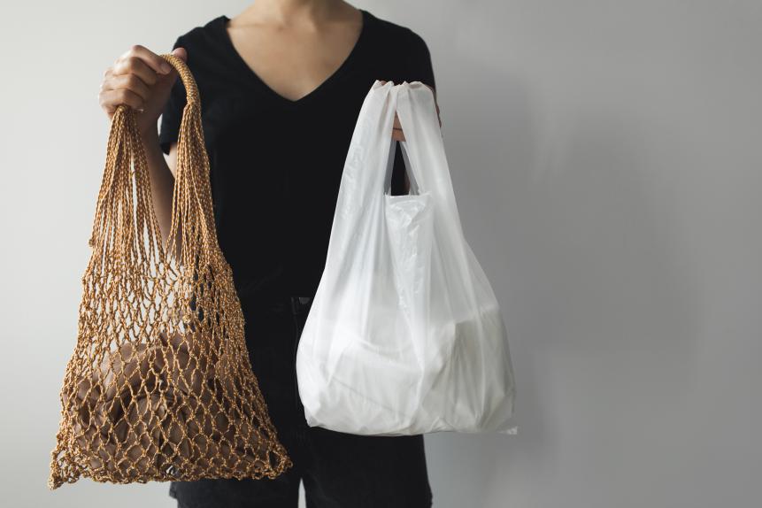 Woman holding mesh eco bag shopper and plastic shopping bags. What you choose: plastic bags or multi-use eco bags. Zero waste concept with copy space.