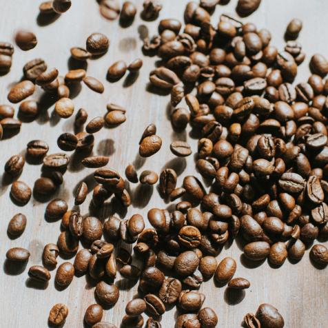 Multitude of brown, whole coffee beans falling on a rustic wooden surface. Background image with space for copy.