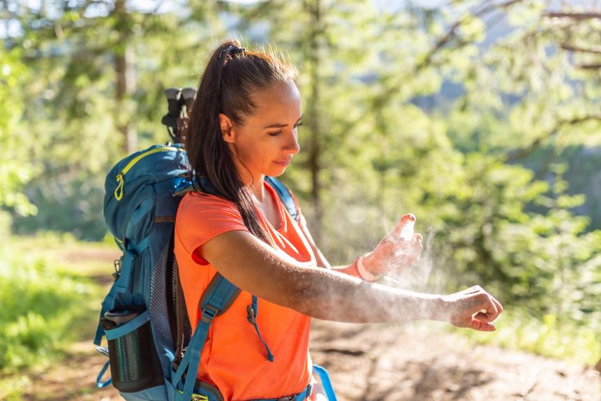 A woman applies mosquito spray to her hands during hiking.