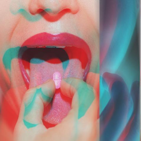 Young woman with colorful psychoactive drug pills on her tongue having psychedelic trip with hallucinations